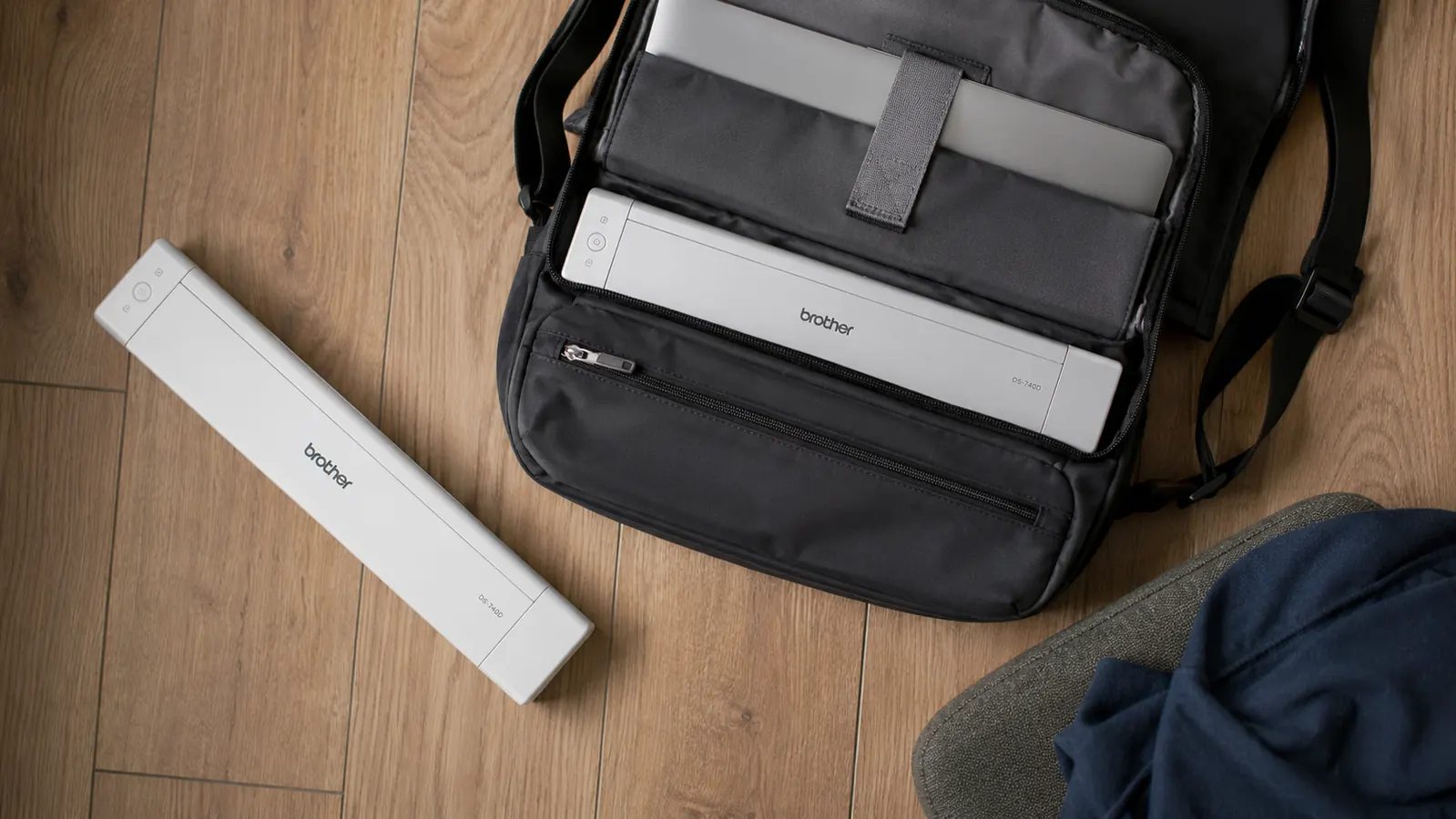 Overhead view of the Brother DS-740D next to a laptop bag, illustrating how compact the scanner is for travel