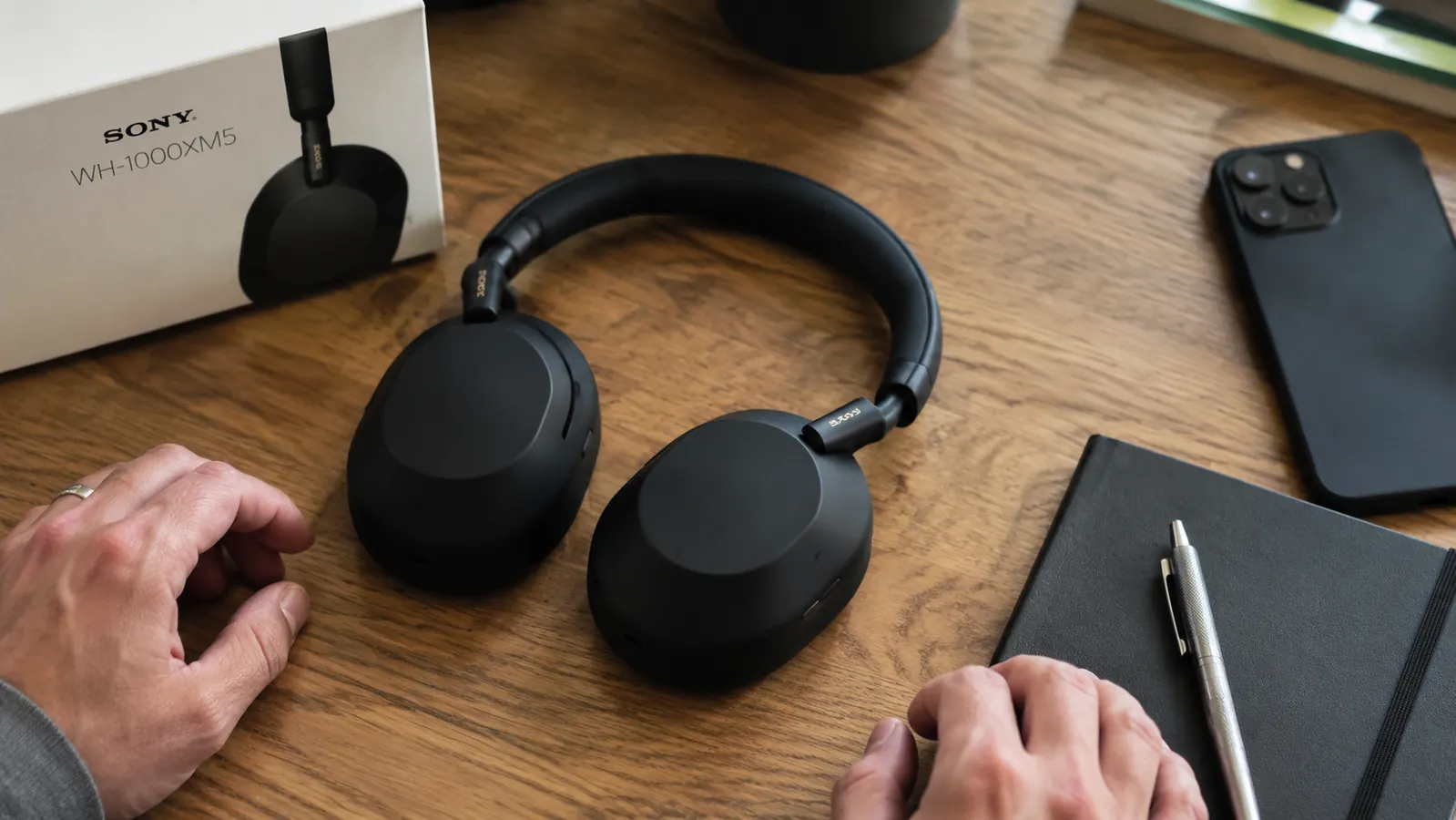 Close-up of Sony WH-1000XM5 headphones resting on a desk next to a notebook and pen