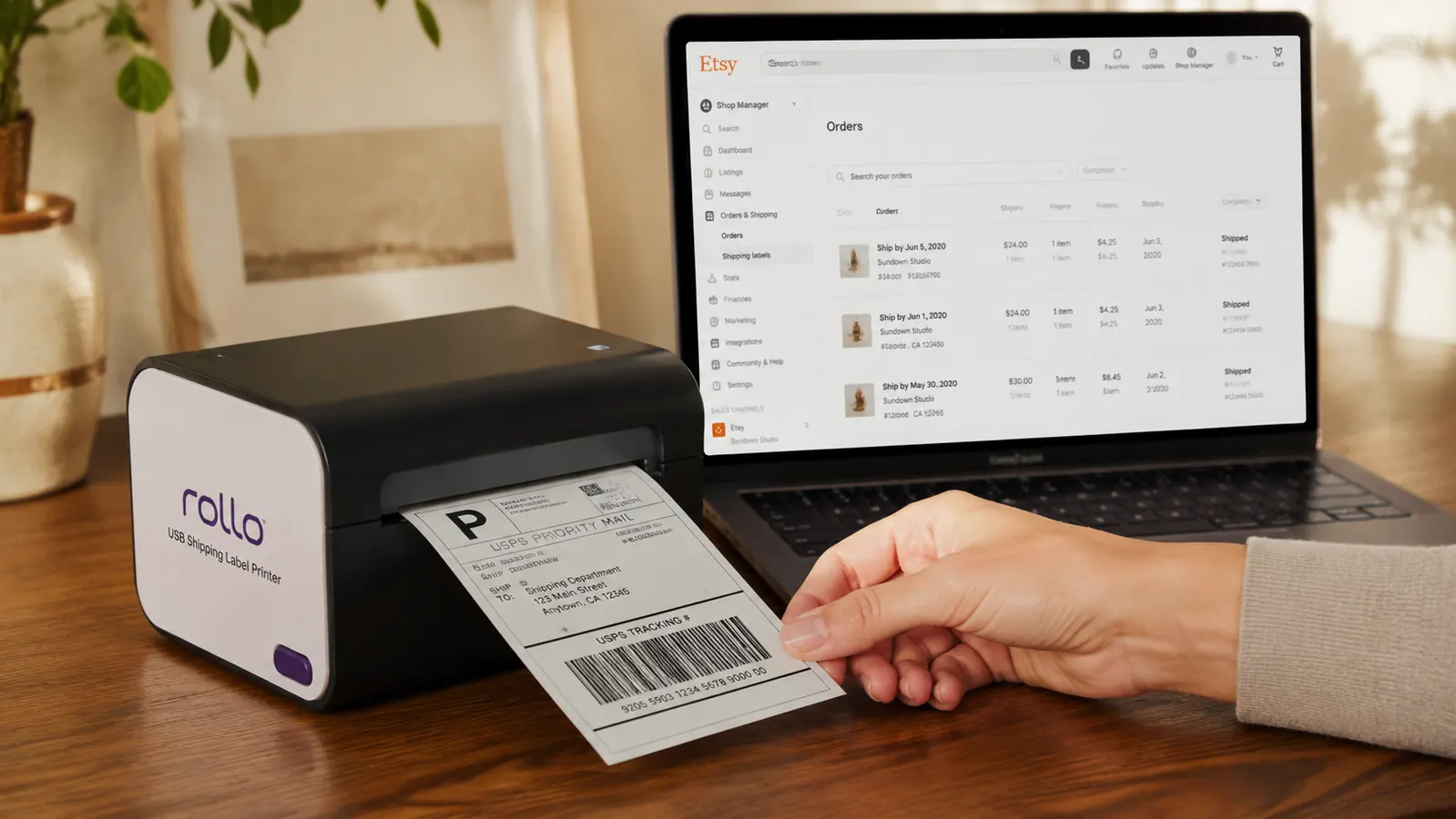 Rollo printer outputting a completed USPS shipping label with a barcode, next to an Etsy order confirmation on a laptop screen