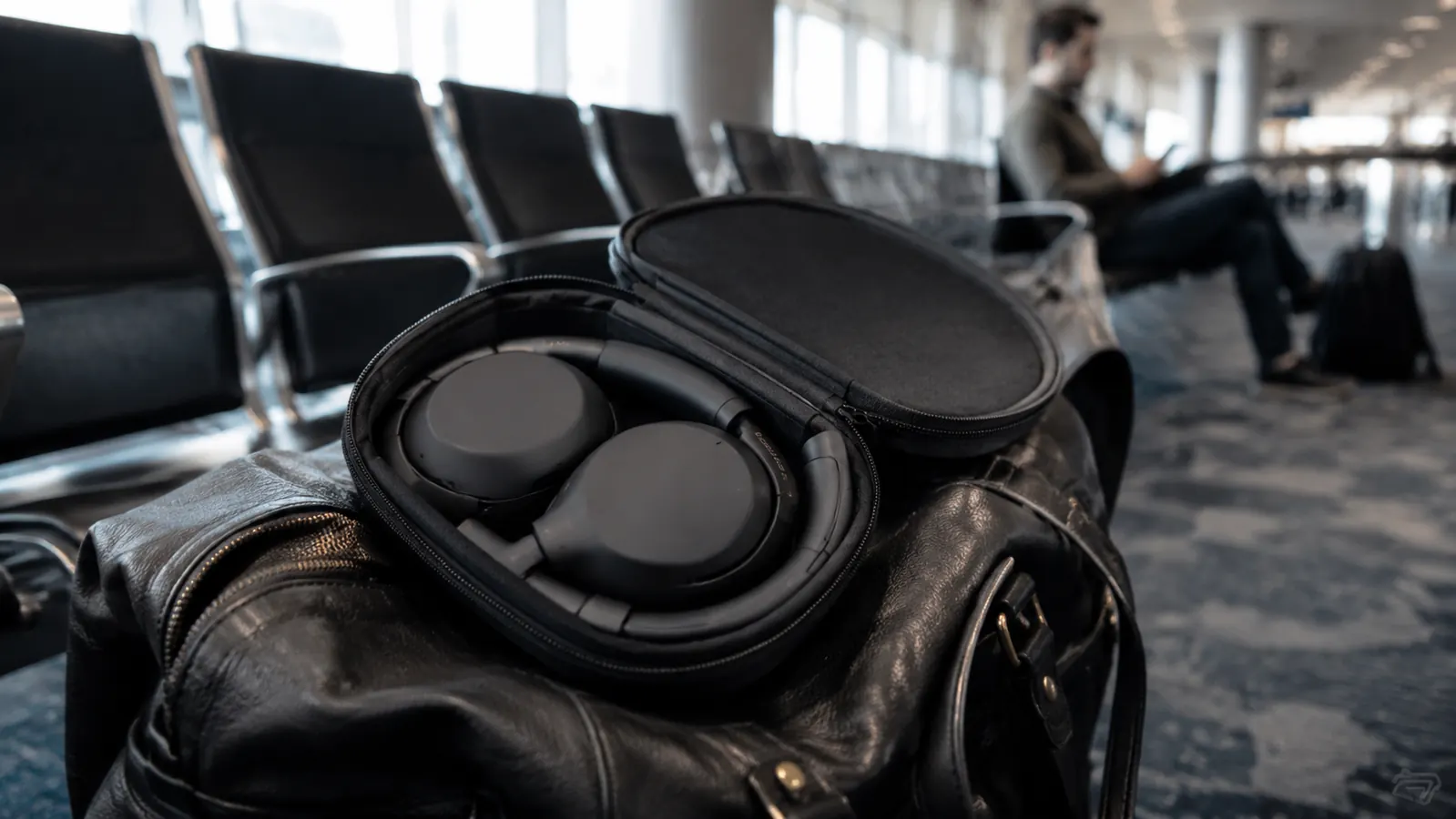 Sony WH-1000XM5 headphones folded in their compact carry case on a traveler's bag